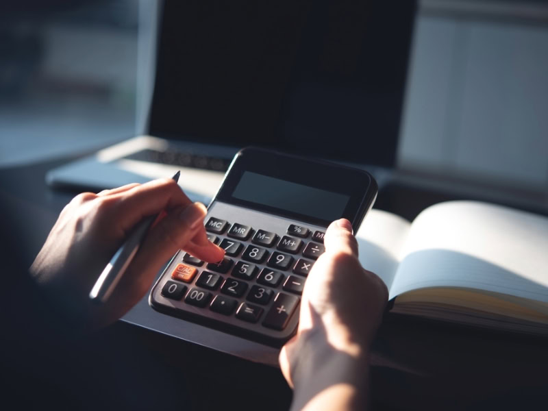 a person using a calculator with a laptop and notebook in view