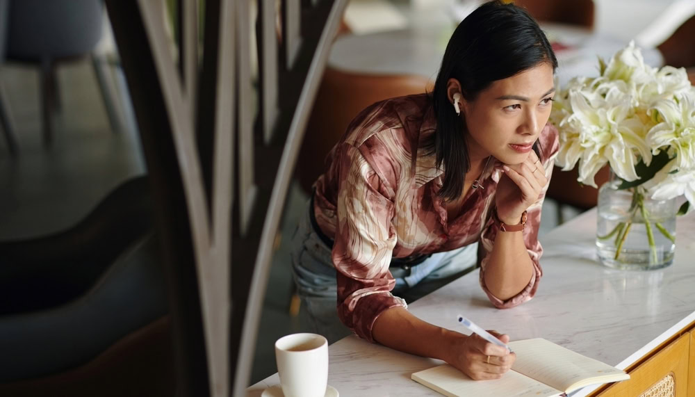 woman contemplating while taking notes