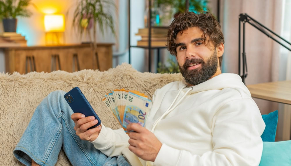 a man sitting on a couch with phone and cash on hand