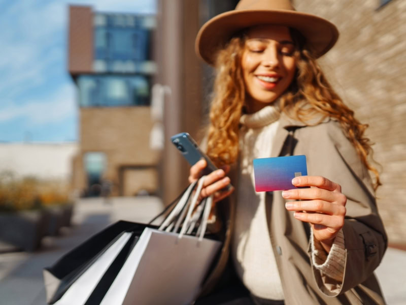 a happy woman holding her shopping bag and looking at the credit card on the other hand